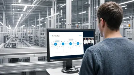 A person sitting in front of a laptop watching a webinar, with an industrial background. 