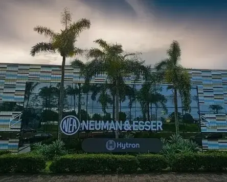 Widok zewnętrzny obiektu NEUMAN & ESSER z oznakowaniem HYTRON, otoczonego palmami.