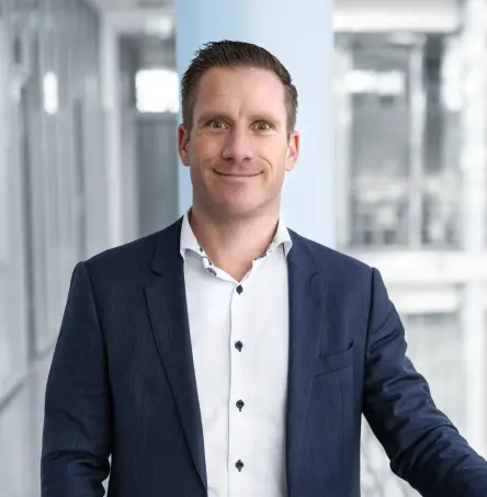 Portrait de Christian Van Boxtel debout dans un couloir de bureau moderne, souriant à l'appareil photo.
