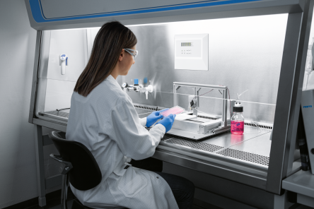Woman in a lab coat sitting at a desk with a microscope
