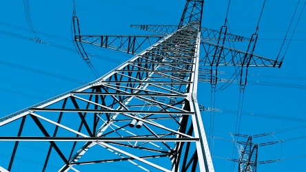 Estrutura metálica de torre de transmissão de energia elétrica vista de baixo para cima, contra um céu azul intenso.