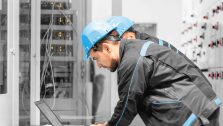 Two maintenance engineers inspecting a relay protection system using a laptop computer