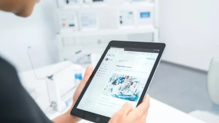 Pessoa segurando um tablet em ambiente corporativo, visualizando uma página com informações técnicas e imagens industriais.